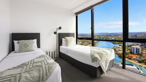 Habitación de hotel con dos camas, un ventanal grande y vista a un paisaje urbano y al agua.