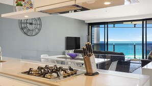 Una cocina moderna con estufa a gas, un reloj y vistas al océano a través de amplios ventanales.