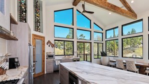 A spacious kitchen with a large island, built-in appliances, and a view of the outdoors through large windows. - Bella Villa: Luxury On Bear Mountain Golf Course! Air Conditioning! Spa! Theatre! Game Room! Walk to slopes! (Big Bear Lake)