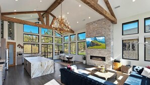 A spacious living area with a fireplace, large windows, and a high ceiling with exposed beams. - Bella Villa: Luxury On Bear Mountain Golf Course! Air Conditioning! Spa! Theatre! Game Room! Walk to slopes! (Big Bear Lake)