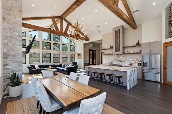 A spacious kitchen with a marble island, wooden beams, and a large dining area with a chandelier.