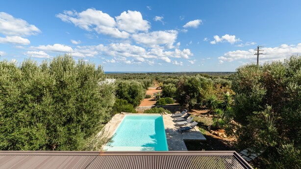 A swimming pool with lounge chairs, surrounded by dense greenery and a clear sky. - Villa Opale by Wonderful Italy (Carovigno)