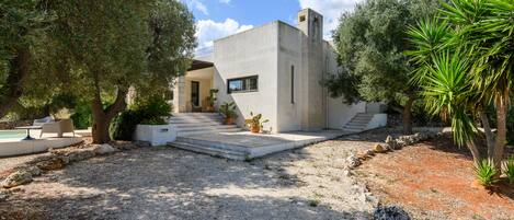 Una casa moderna con fachada de concreto, una escalera de piedra que lleva a la entrada y un camino de acceso de grava.