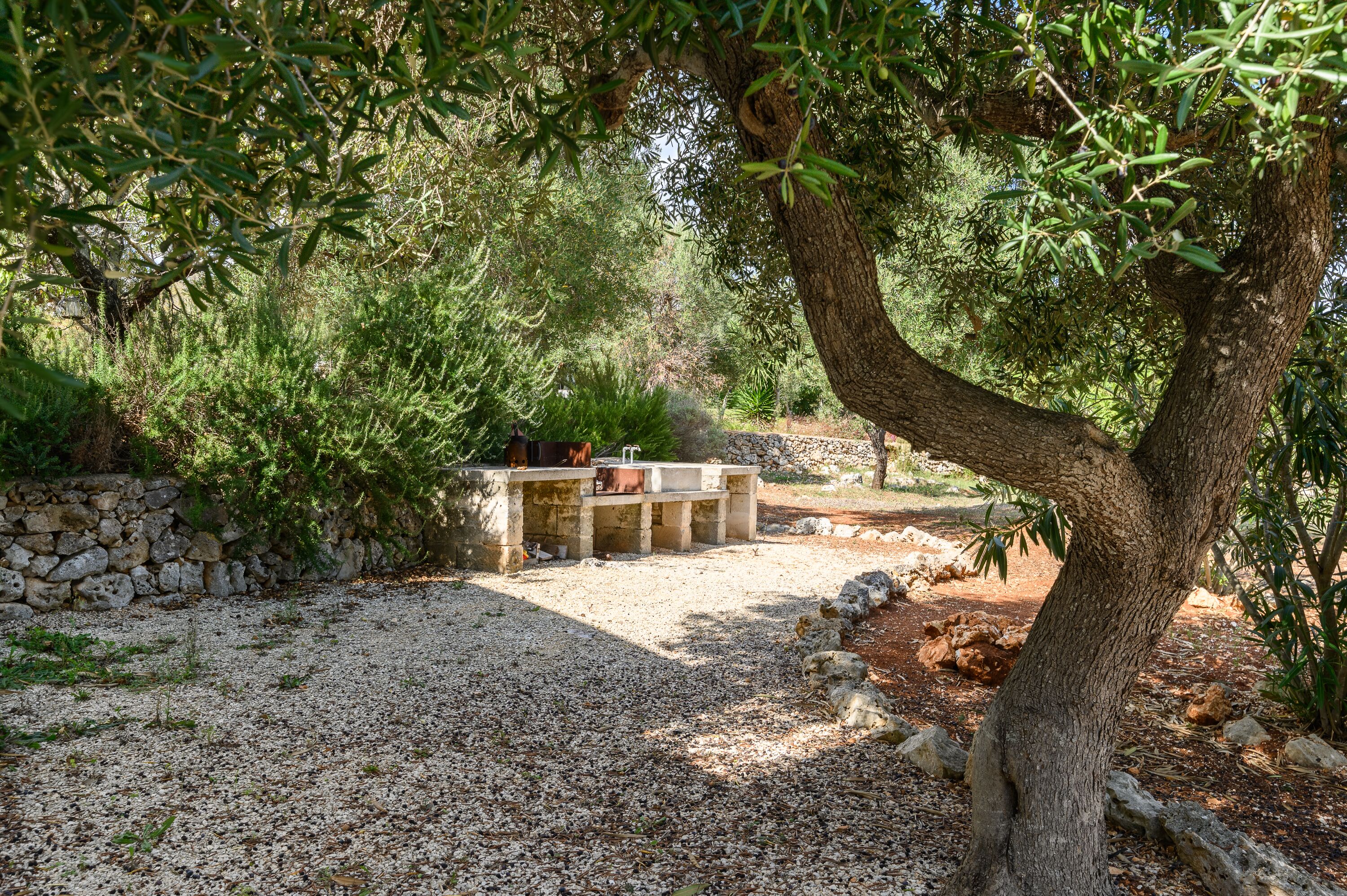 A stone wall, a seating area with a table and chairs, and a gravel path.