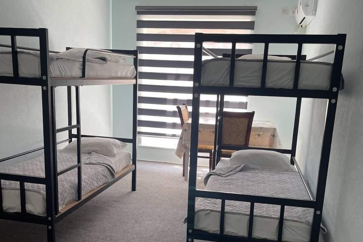 A room with bunk beds, a window with blinds, and a ceiling fan.