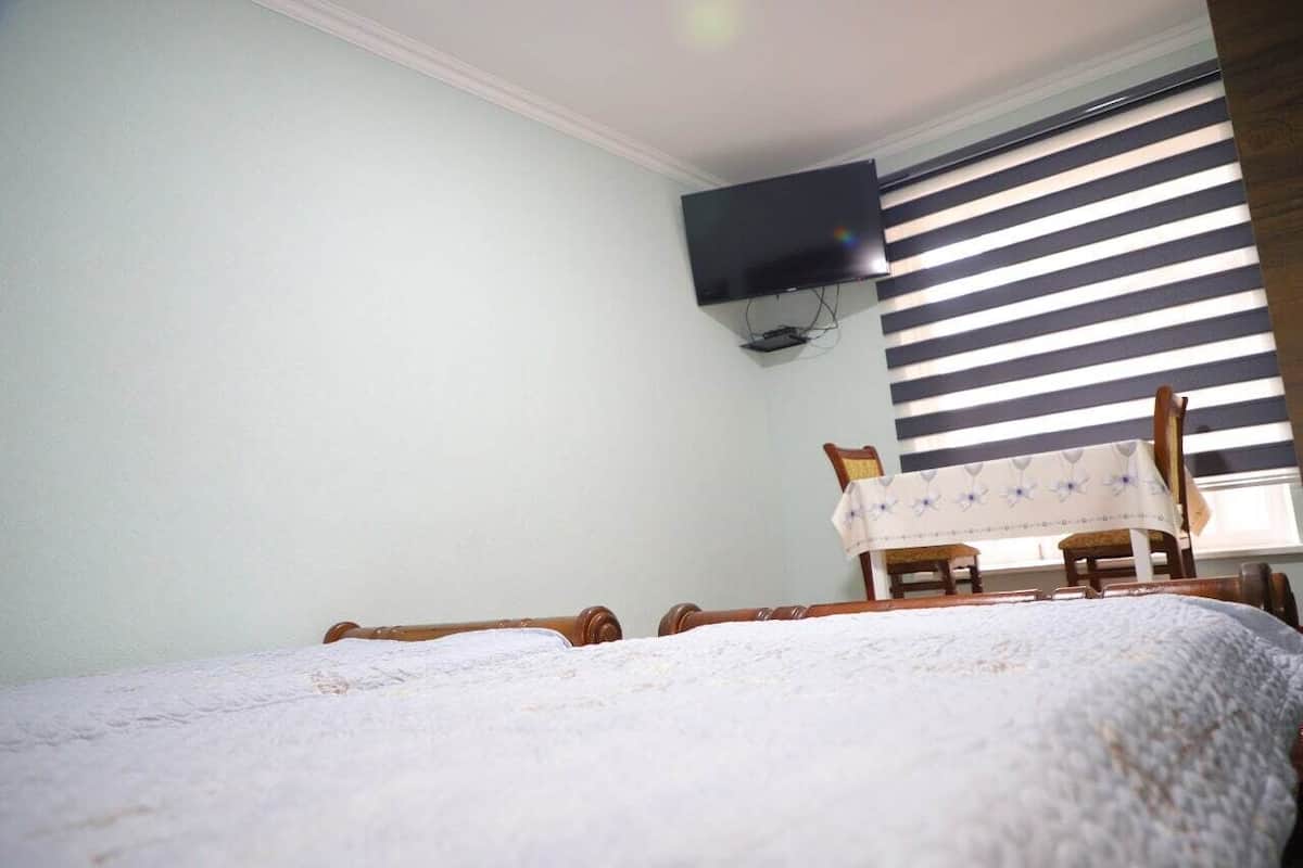 A bedroom with a bed, a desk, and a TV mounted on the wall.