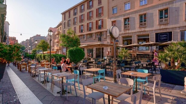 An outdoor café with tables and chairs, surrounded by buildings with balconies and windows. - Suite nel Largo (Cagliari)