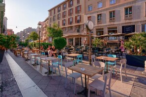 Een terras met tafels en stoelen, omgeven door gebouwen met balkons en ramen.