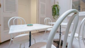 A room with a white table and chairs, a hanging plant, and a window with blinds. - Suite nel Largo (Cagliari)