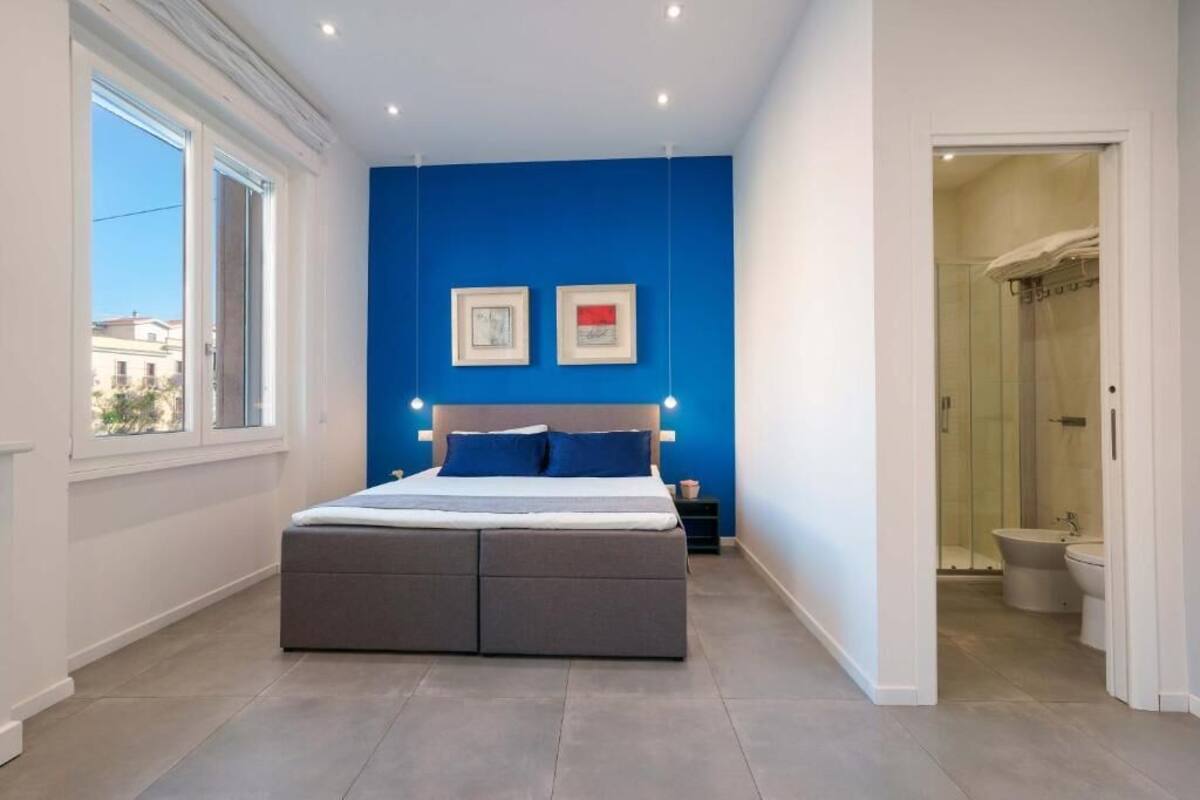 Un dormitorio moderno con una cama grande, una pared azul de acento y vistas de la ciudad a través de una ventana.