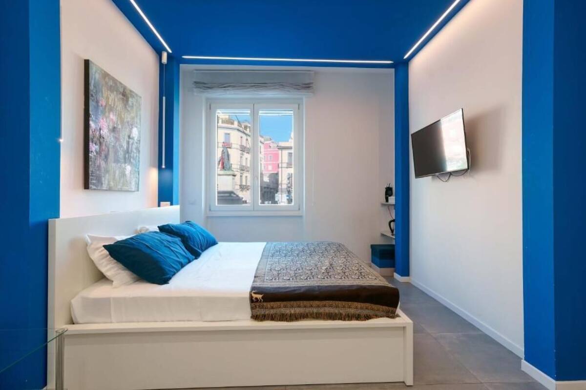 Un dormitorio con cama, televisión, ventana y un cuadro en la pared.