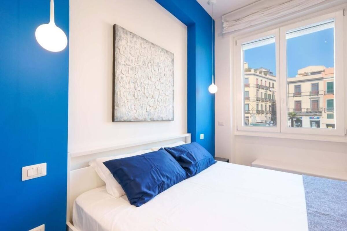 Un dormitorio con cama, un ventanal grande y una obra de arte colgada en la pared.