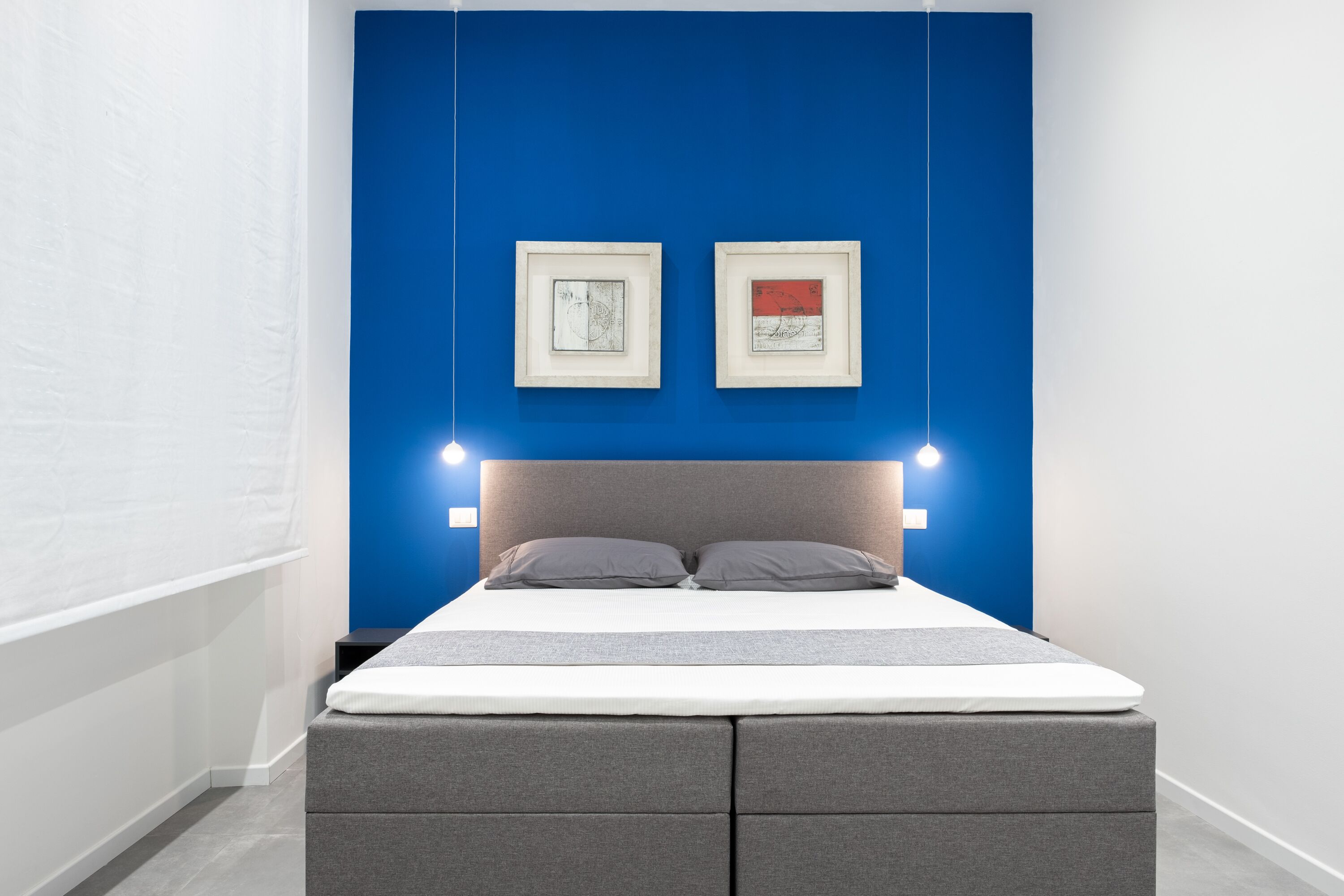 A modern bedroom with a blue accent wall, a grey upholstered bed, and two framed artworks.
