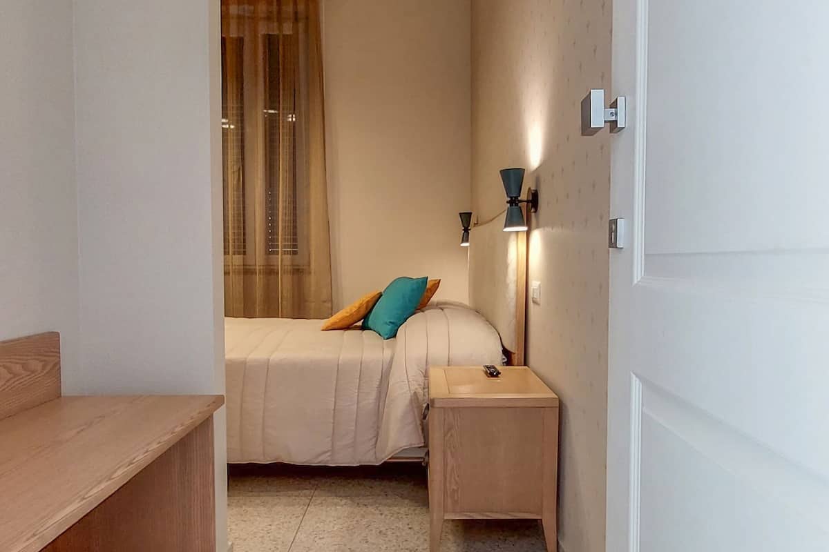 A small, compact room with a bed, bedside table, and a desk.