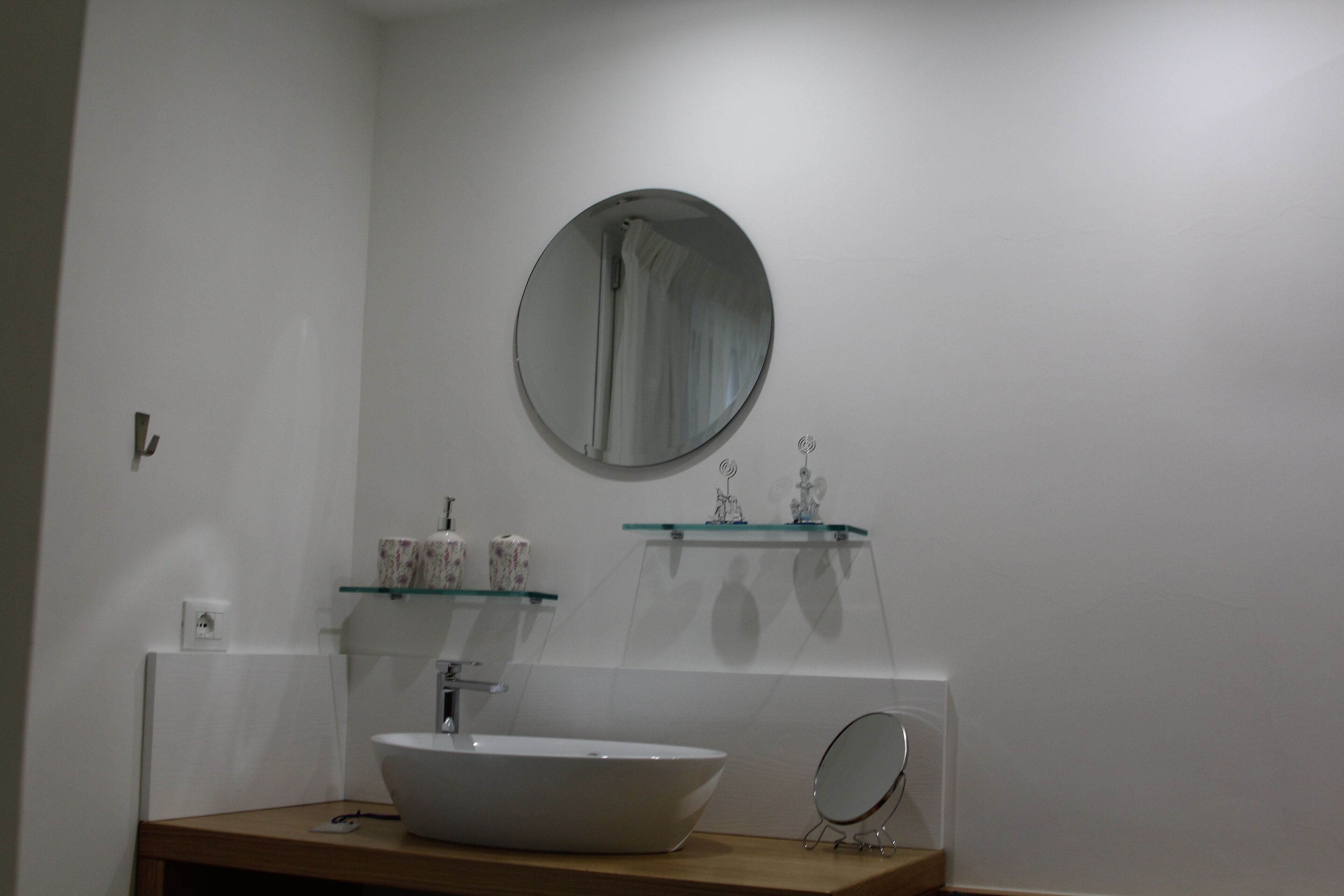 A bathroom with a white sink, a round mirror, and two glass shelves with toiletries.