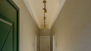 Un pasillo con una puerta verde a la izquierda, un accesorio de iluminación colgando del techo y una puerta al final.