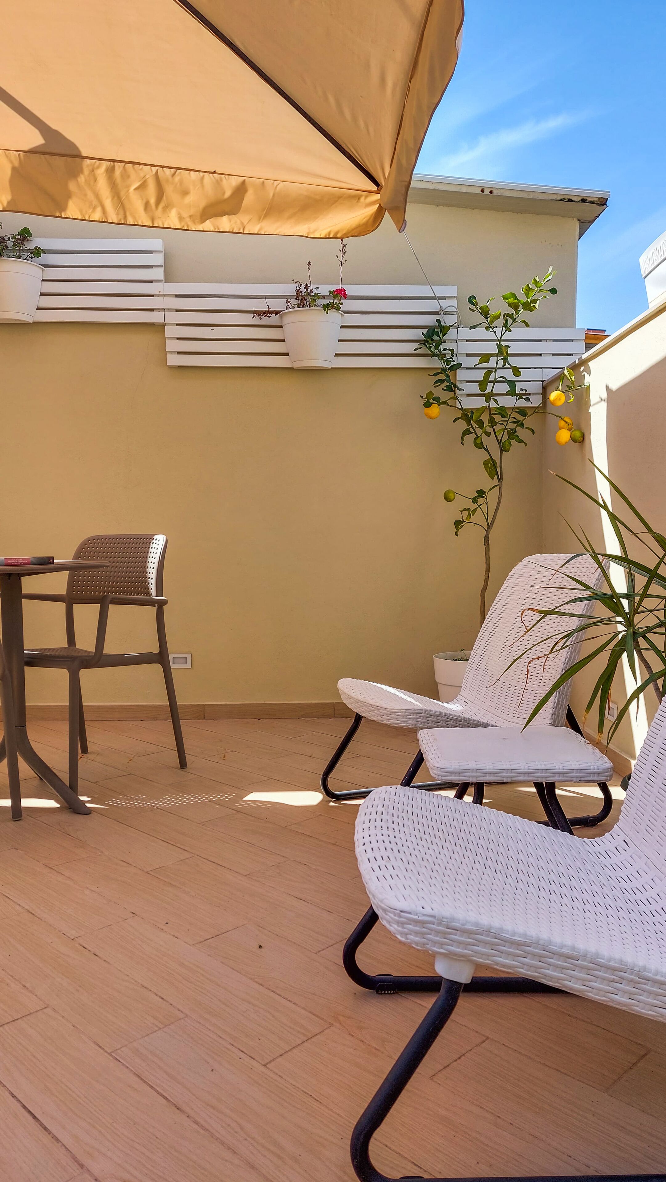 A balcony with a table and two chairs, a hanging plant, and a white railing.
