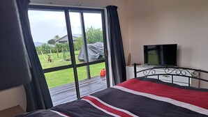 Quarto com cama grande, televisão e vista para uma área verde lá fora.