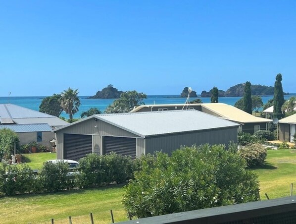 A residential area with houses, a clear blue sky, and a view of the sea with islands in the distance. - Bland Bay Bach (Whangaruru)