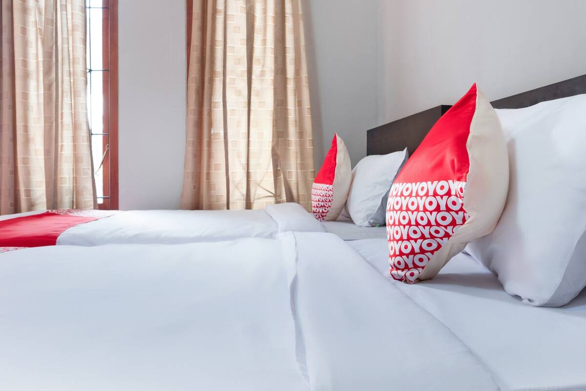 Una habitación de hotel con una cama bien hecha, cortinas color crema y una ventana con vistas.