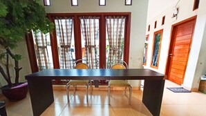 Un coin repas avec une longue table et des chaises, une plante en pot et une vue par une fenêtre ornée de rideaux.