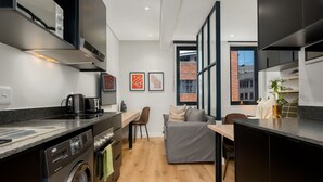 A compact kitchen with modern appliances, a dining area, and a view of the city through large windows.