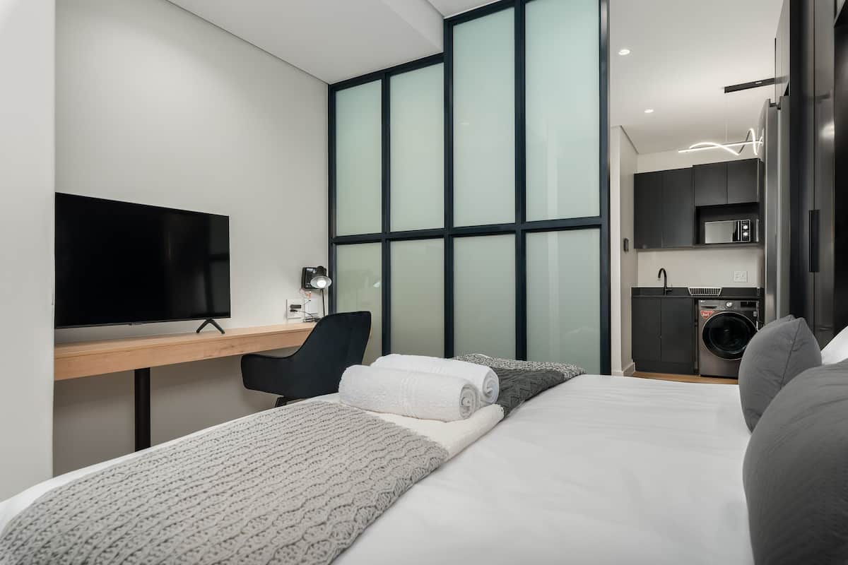 Habitación de hotel moderna con una cama grande, un escritorio con televisor, una silla y una lavadora en la esquina.