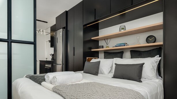 A modern bedroom with a large bed, dark cabinetry, and a wooden shelf with books and a clock.