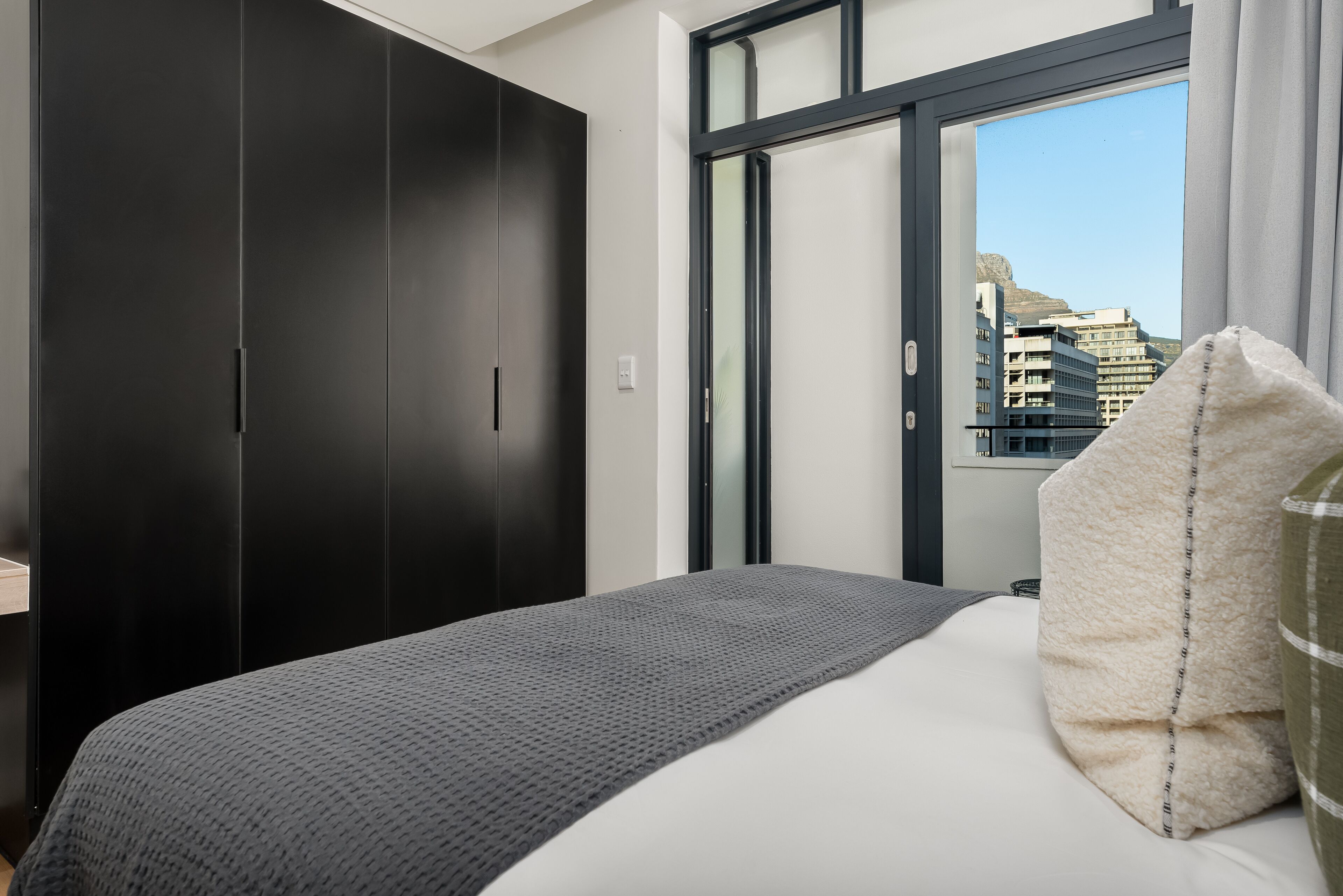 Quarto de hotel com cama, guarda-roupa escuro, janela com vista para edifícios e cortina.