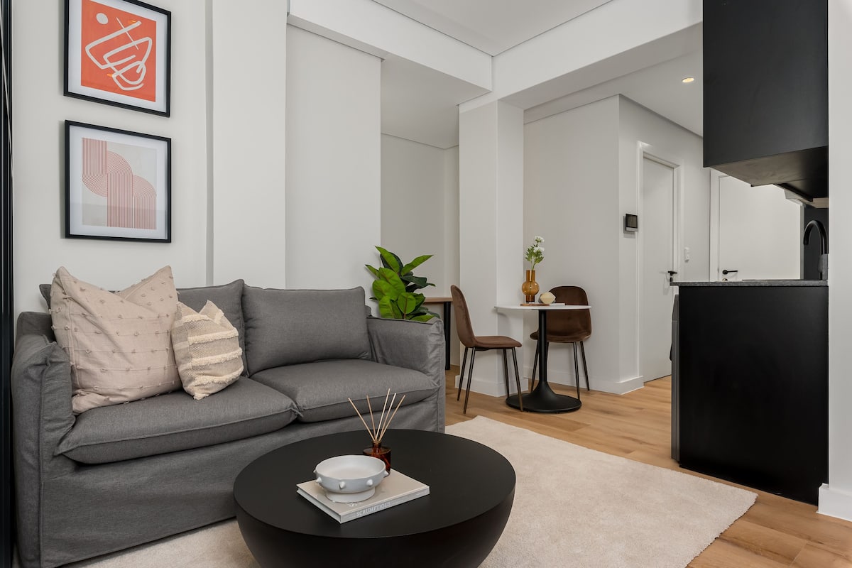 Una sala de estar moderna con un sofá gris, una mesa de centro negra y dos obras de arte abstractas enmarcadas.
