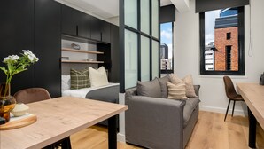 A modern apartment with a dining area, a sofa, a bed, and a large window with a city view.