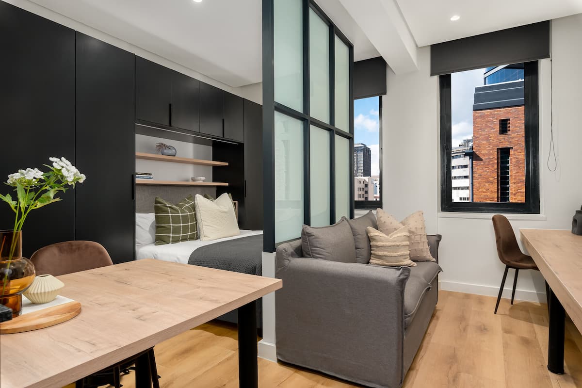 Un apartamento moderno con comedor, sofá, cama y un ventanal con vistas a la ciudad.