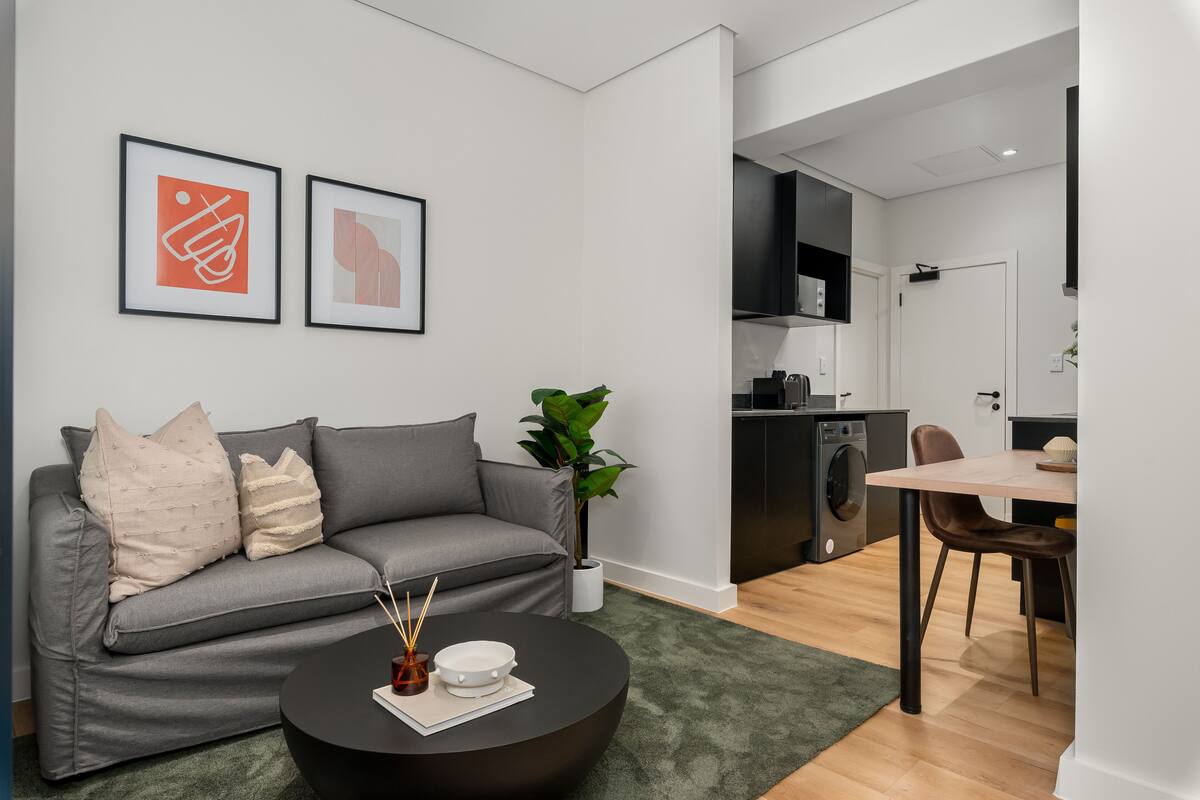 Un salón moderno con un sofá gris, una mesa de centro negra y dos cuadros enmarcados en la pared.