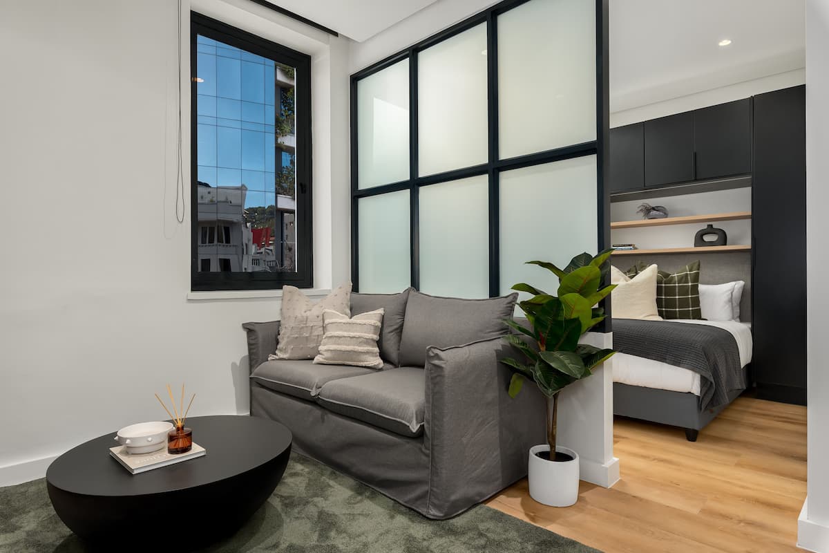 Una sala de estar moderna con un sofá gris, una mesa de centro negra y un ventanal grande.