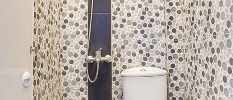 A bathroom with a toilet, shower, and tiled walls with a polka dot pattern.