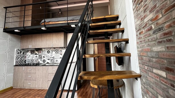 Ein modernes Interieur mit einer Holztreppe, einem Schlafzimmer im oberen Bereich und einer Küche mit gemusterten Fliesen.