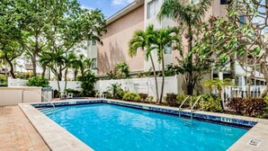 A rectangular swimming pool with a blue tiled edge, surrounded by a brick patio. - Bayway Shores 303 - Waterfront Condo (CLEARWATER BEACH)