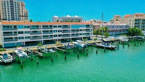 A marina with boats docked, a multi-story building with balconies, and a clear blue sky. - Bayway Shores 303 - Waterfront Condo (CLEARWATER BEACH)