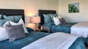 A hotel room with two beds, each with teal bedding and multiple pillows. There is a bedside table with a lamp and a small plant. - Bayway Shores 303 - Waterfront Condo (CLEARWATER BEACH)