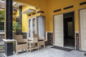 A yellow exterior with a glass door entrance, a stone pillar, and a wicker table with chairs.