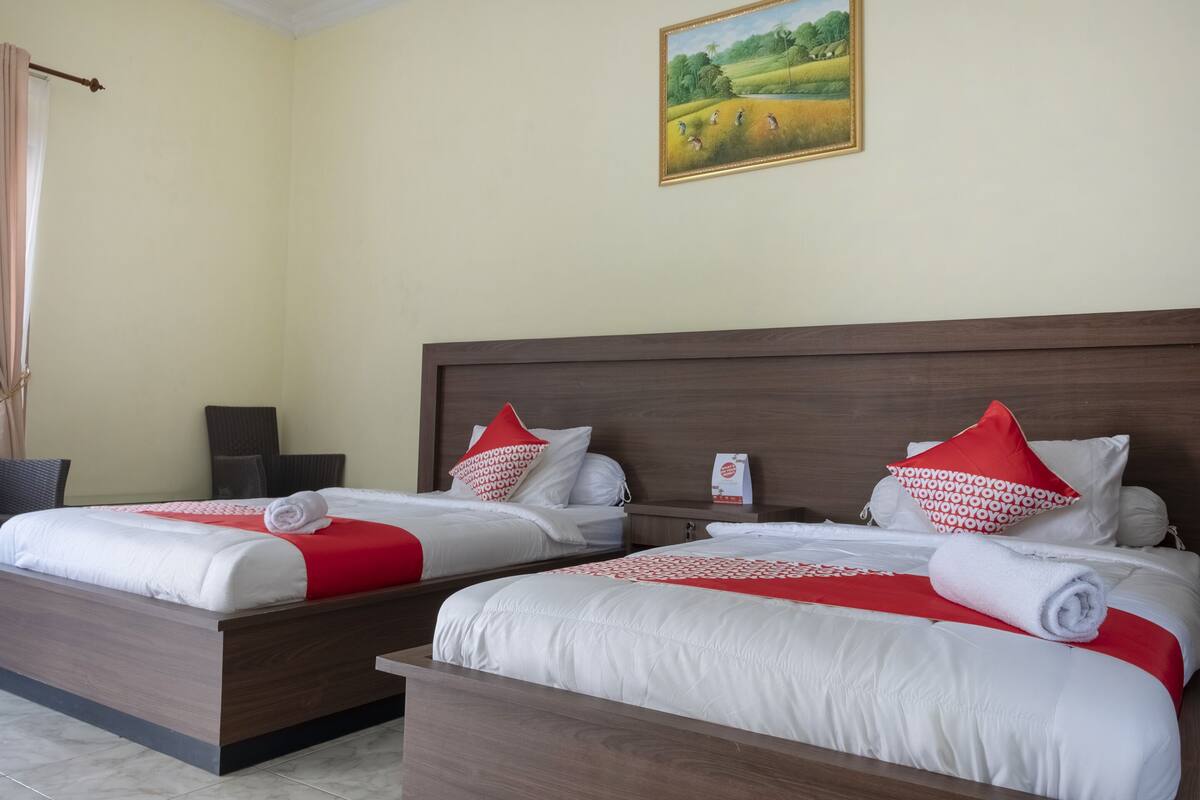 A hotel room with two beds, each with white bedding and red accents, a wooden headboard, and a painting of a landscape on the wall.