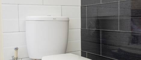 A bathroom with a white toilet, a black tiled wall, and a white tiled floor.