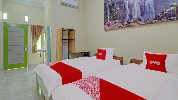 A hotel room with two beds, a green door, a white air conditioner, a wooden cabinet, and a large waterfall painting on the wall.