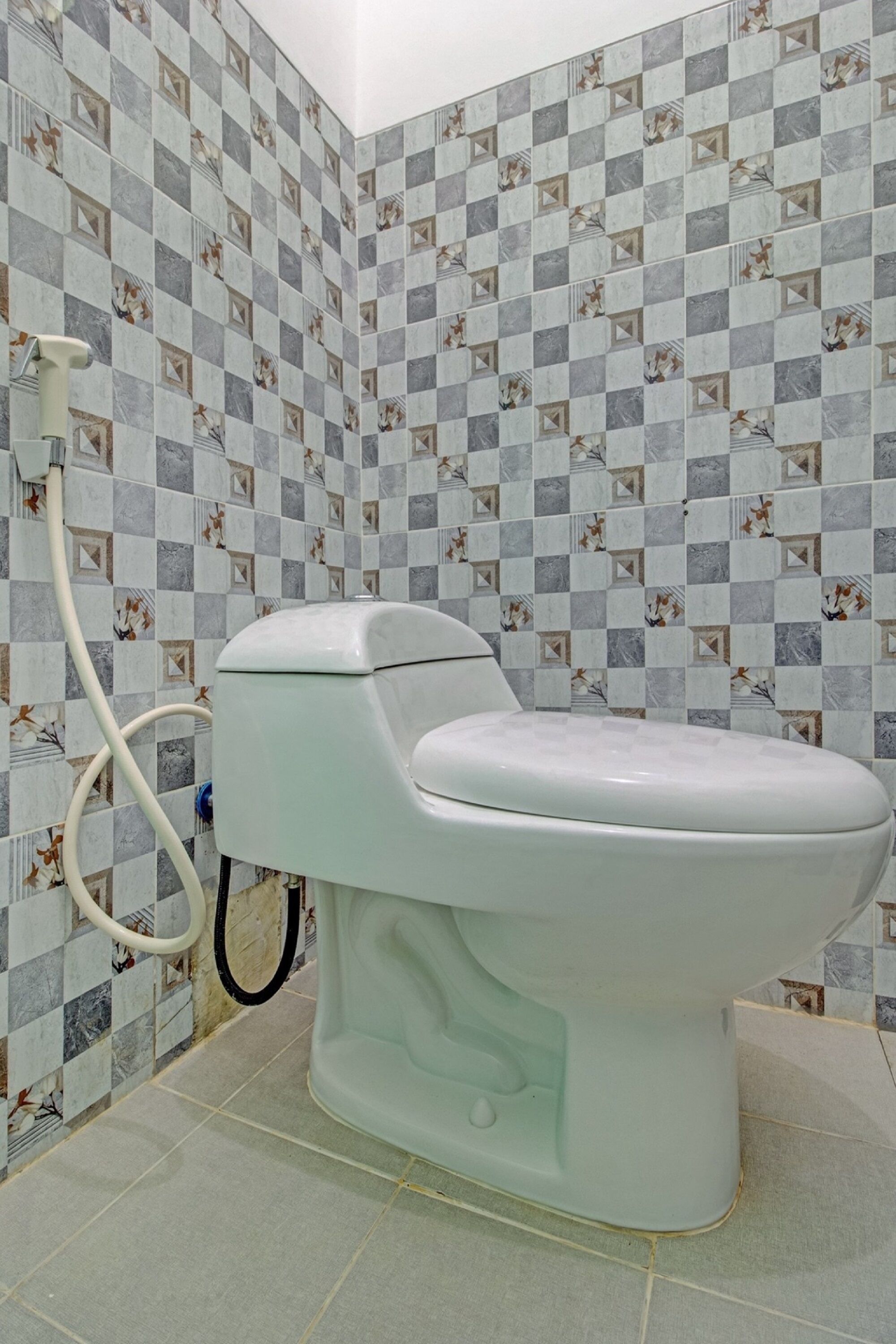 A bathroom with a toilet, a shower hose, and patterned tiles on the walls.