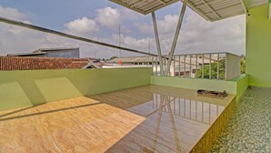 A rooftop terrace with a wooden floor, a metal roof, and a view of buildings in the background.
