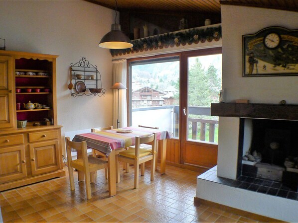 A cozy dining area with a wooden table and chairs, a cabinet with dishes, a hanging light, and a fireplace.