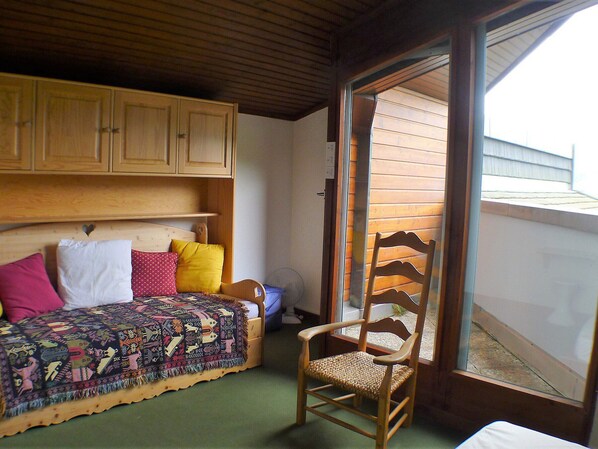 A small, cozy room with a wooden bed, a chair, and a window with blinds. - Comfortable & bright 2-room in Samoëns center - Pets allowed and parking included (Samoëns)