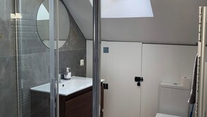 A modern bathroom with a glass shower enclosure, a white sink, a wooden vanity, a toilet, and a skylight.