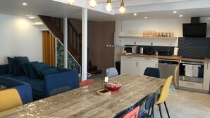 A modern kitchen with a dining area, a staircase, and a living room with a sofa and chairs.