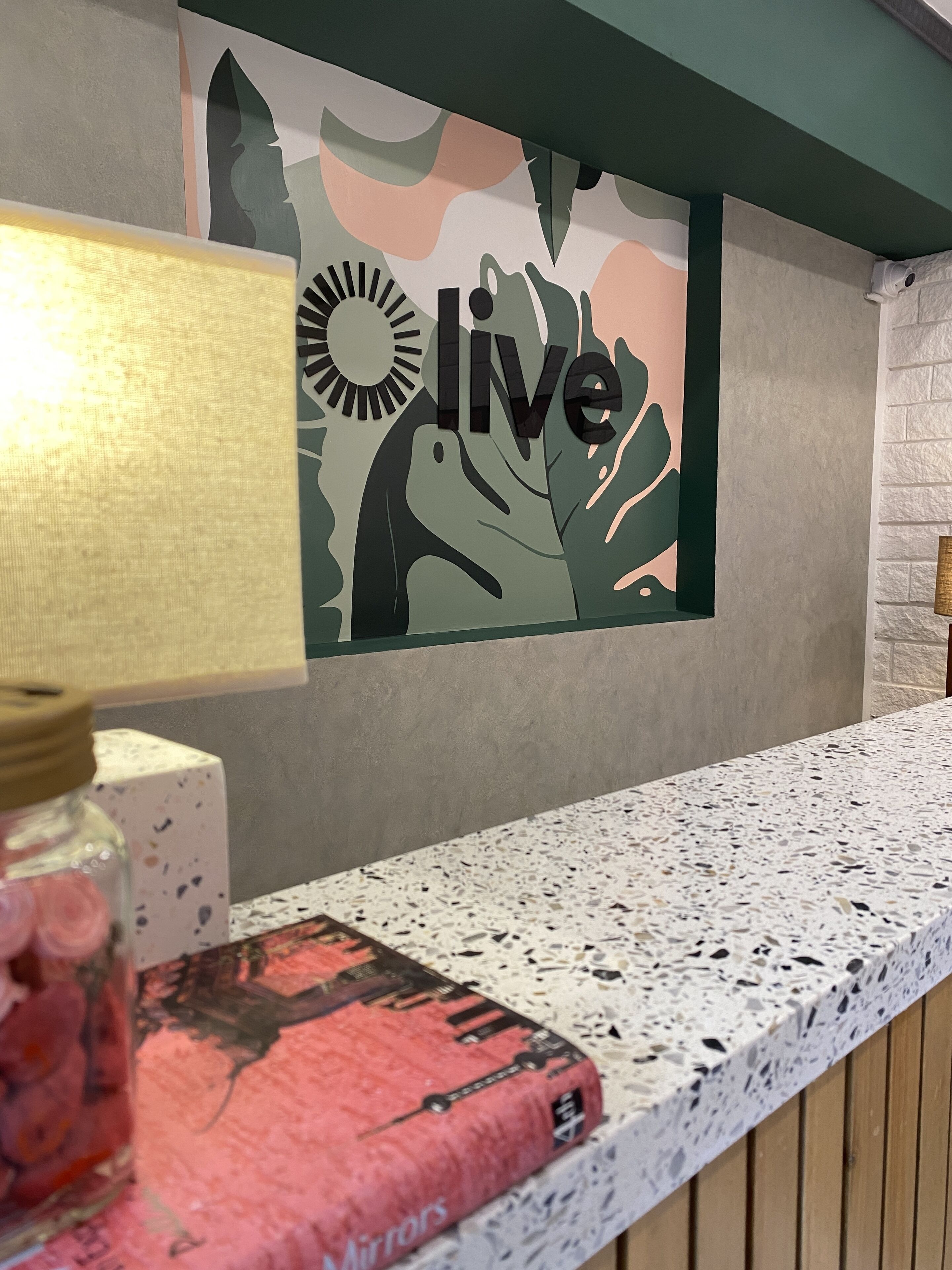 Ein Empfangsschalter mit einem Schild mit der Aufschrift 'live', einer Wand mit Muster und einer Lampe.